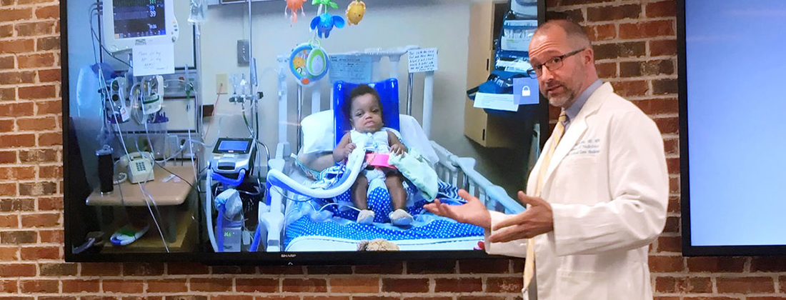 Doctor stands in front of tv screen showing patient Xavier