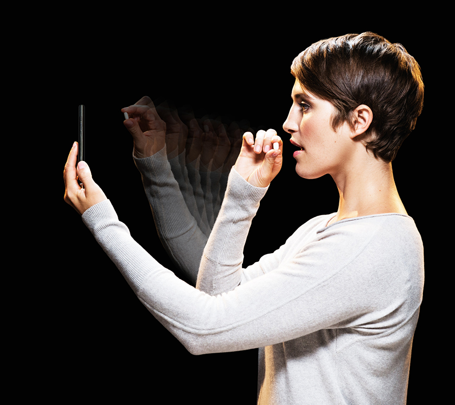 A woman holds a pill up to a smartphone and prepares to take the pill