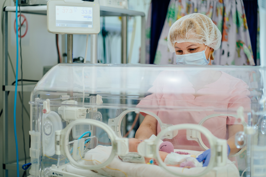 Doctor checks on new born infant lying in an incubator.