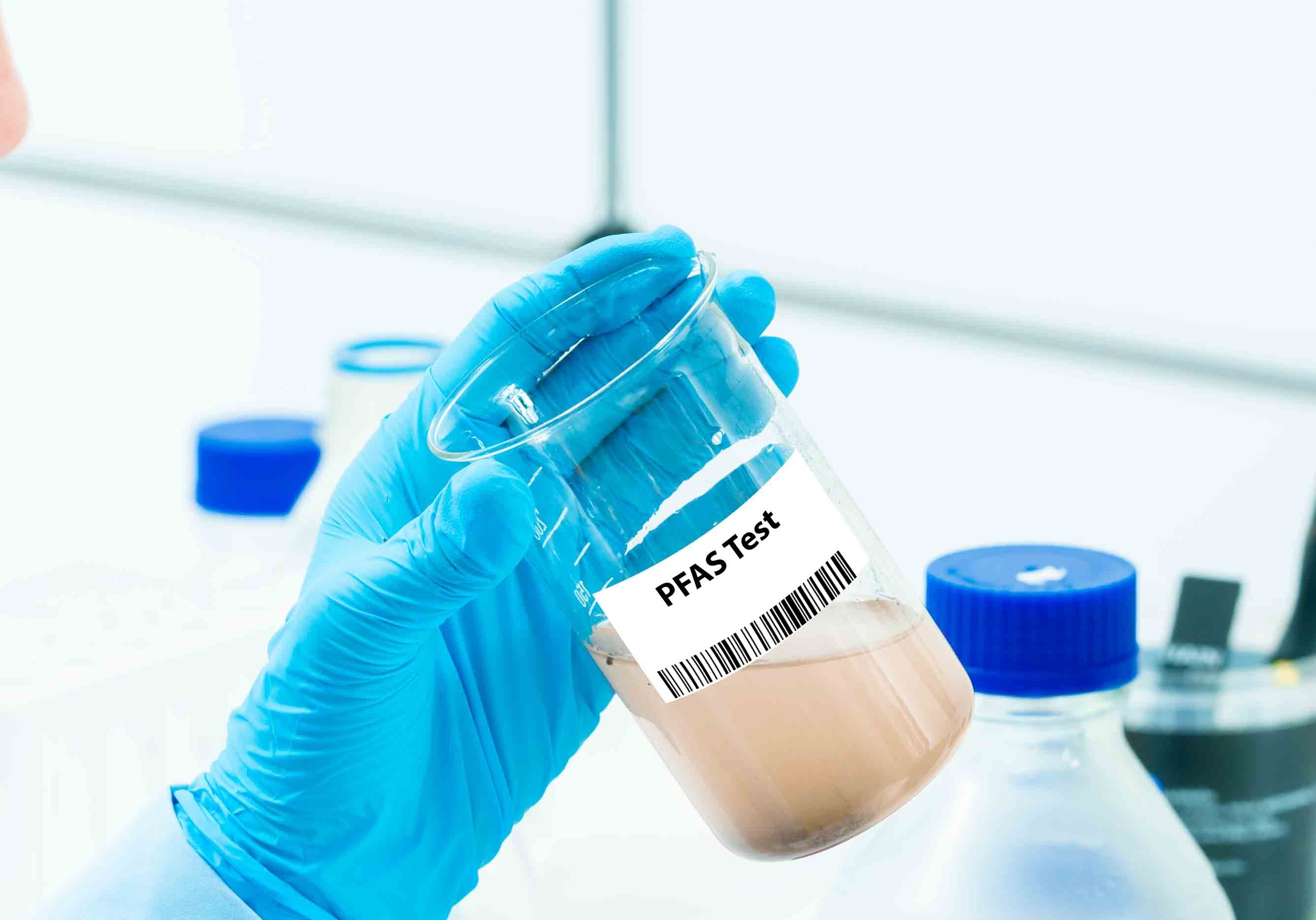 Gloved hand holds beaker containing liquid and a label that reads, “PFAS Test.”
