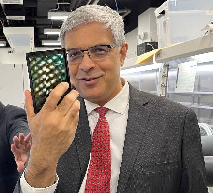 A man in a suit holds a well plate with a pixelated image of himself up to the camera while smiling.