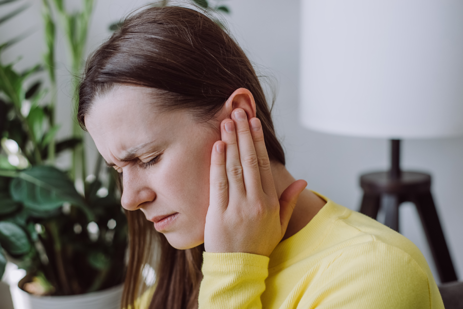 Young woman holding her ear while grimacing with pain.