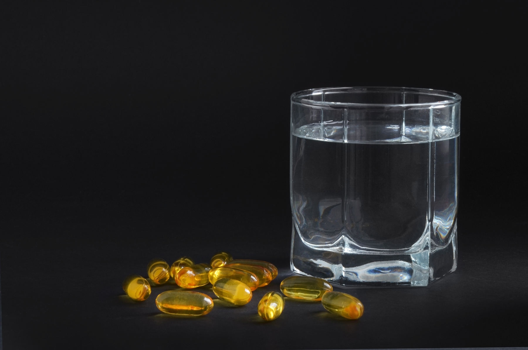 A glass of water next to a small pile of yellow gel capsules.