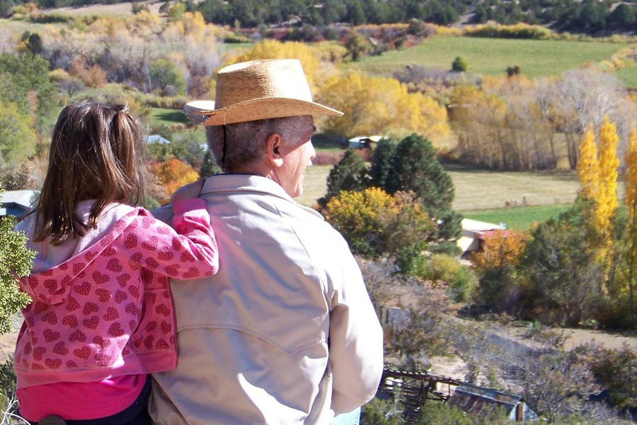Older man and young girl sitting side-by-side looking at rural farmland.