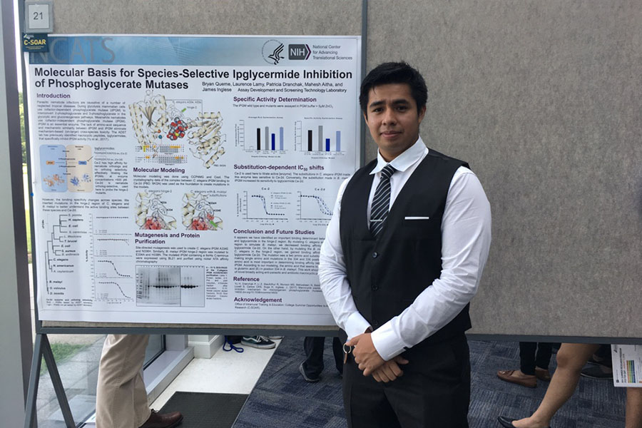 Bryan Queme in front of a poster display titled "Molecular Basis for Species-Selective Ipglycermide Inhibition of Phosphoglycerate Mutases"
