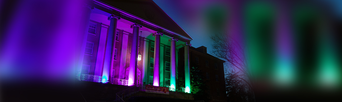 NIH Building 1 lit up at night with Rare Disease Day colors.