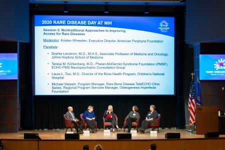 The moderator and four panelists from the session “Nontraditional Approaches to Improving Access for Rare Diseases” talk in front of a large slide projection at Rare Disease Day at NIH 2020.