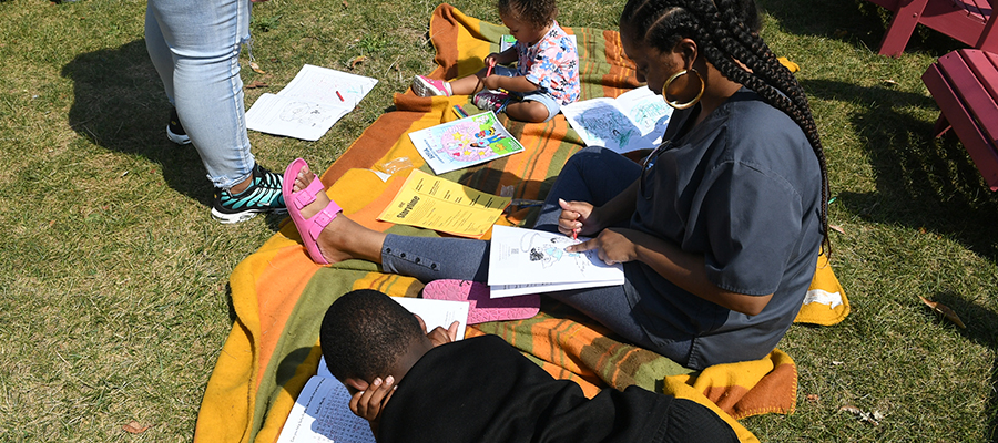 A family sits on a blanket coloring pages from the “Sofia Learns About Research” activity book.