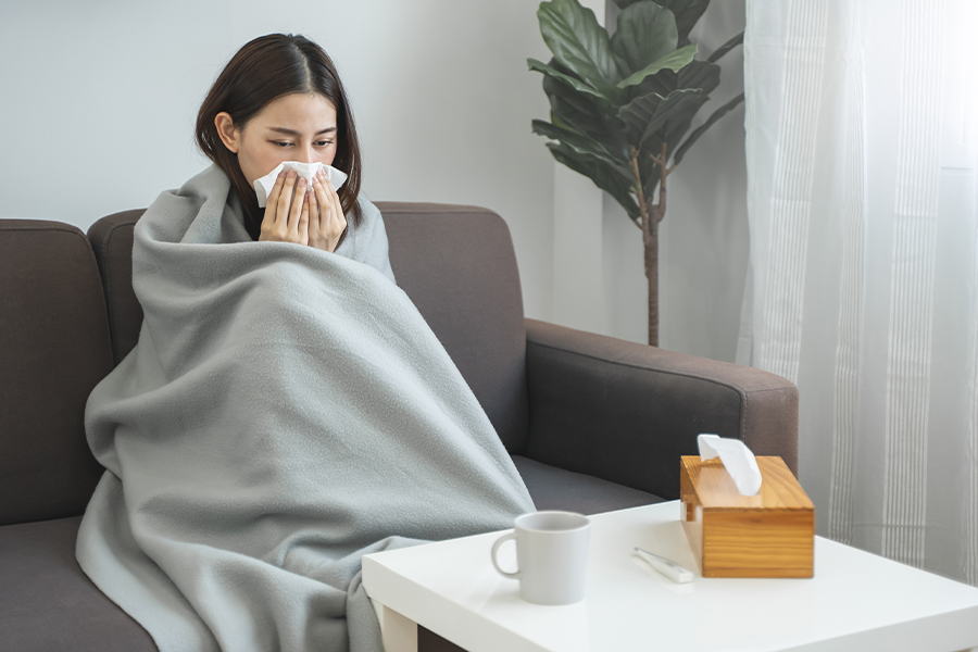 Photograph of a woman with a common cold wrapped in a blanket blowing her nose.