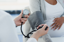 Physician uses blood pressure monitor on pregnant individual.