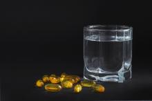 Glass of water next to a small pile of yellow gel capsules.