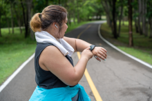 Young overweight woman checking the result of her morning run on her smart watch while standing at a running track of a local park