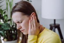 Young woman holding her ear while grimacing with pain.