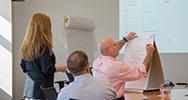 Two people looking at one person writing on a flip-top easel.